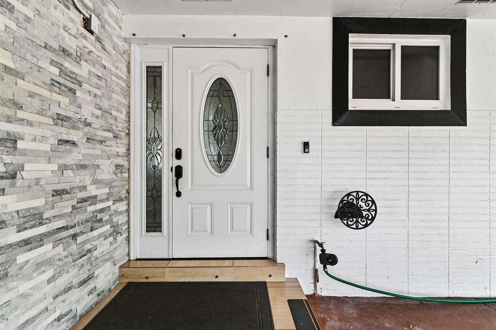 A white front door with a glass oval insert sits beside a stone-tiled wall — 124 Davis Road, Palm Springs FL 33461, PALM SPRINGS, FL