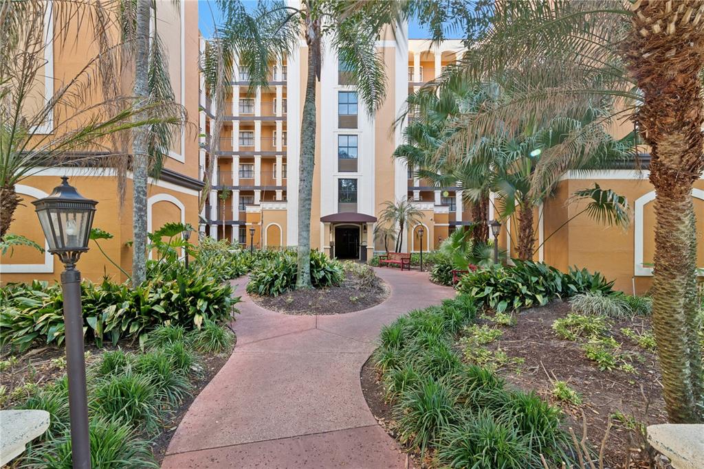 A paved walkway leads through a landscaped courtyard toward the entrance of a multi-story building — 12538 FLORIDAYS RESORT DRIVE UNIT 602C, ORLANDO, FL