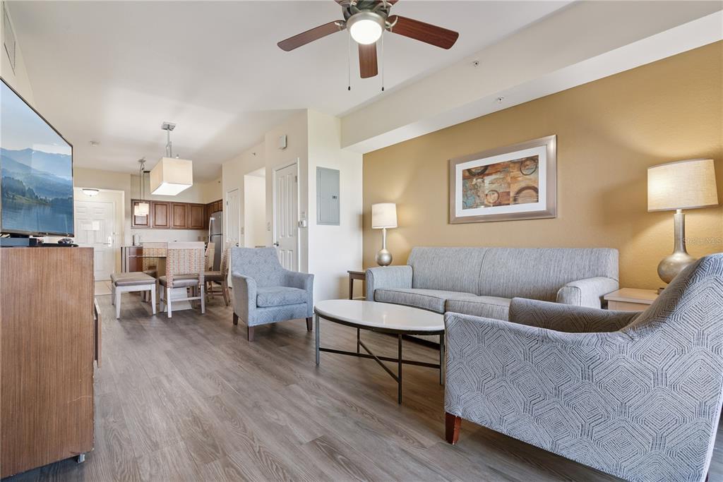 A living room with wood-look flooring, a gray sofa, two armchairs, and an open kitchen — 12538 FLORIDAYS RESORT DRIVE UNIT 602C, ORLANDO, FL