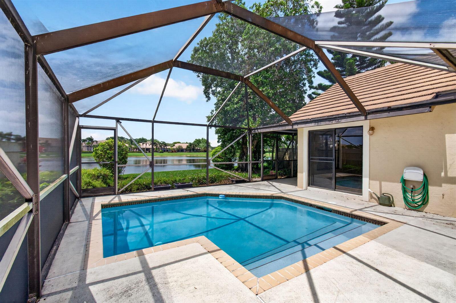 A screened-in patio features a swimming pool overlooking a lake and residential neighborhood — 7004 Bitterbush Place, Boynton Beach FL 33472, BOYNTON BEACH, FL