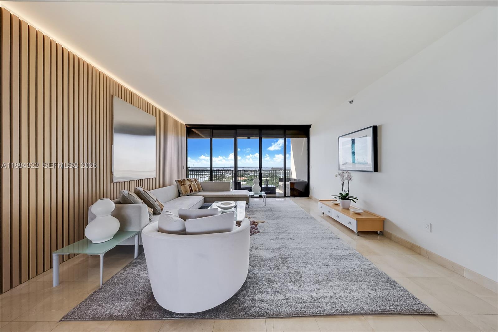A modern living room features a slatted wood wall, a large area rug, and balcony views — 1000 Venetian Way # 1902, Miami FL 33139, MIAMI, FL