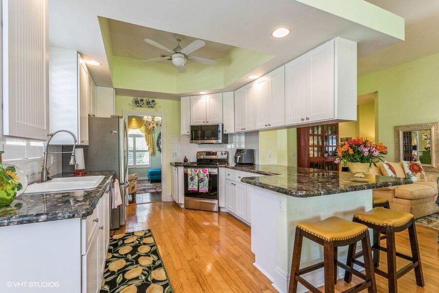 A kitchen with white cabinets, granite countertops, hardwood floors, and a breakfast bar — 170 Euphrates Circle, Palm Beach Gardens FL 33410, PALM BEACH GARDENS, FL