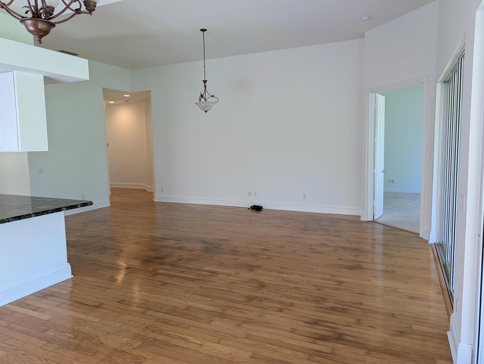 An empty room with hardwood floors, a hanging light fixture, and an open doorway — 170 Euphrates Circle, Palm Beach Gardens FL 33410, PALM BEACH GARDENS, FL