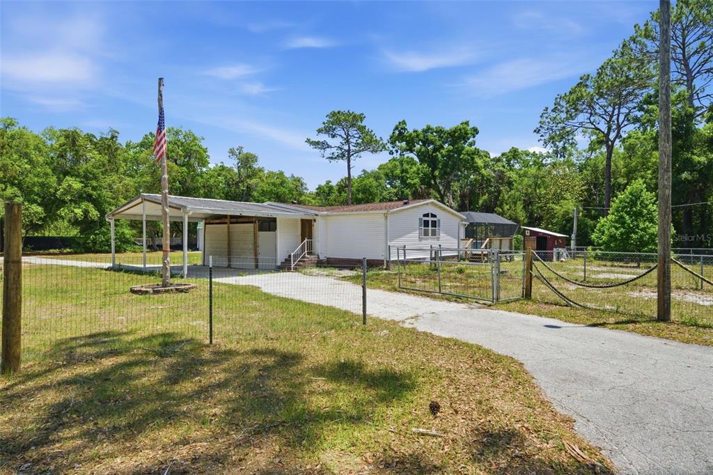 A single-story mobile home with a carport, fenced yard, and a gravel driveway — 2295 S STONEBROOK DRIVE, HOMOSASSA, FL
