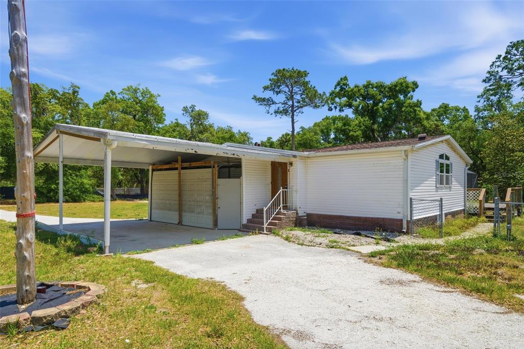 A single-story house with white siding and an attached carport sits on a grassy lot — 2295 S STONEBROOK DRIVE, HOMOSASSA, FL