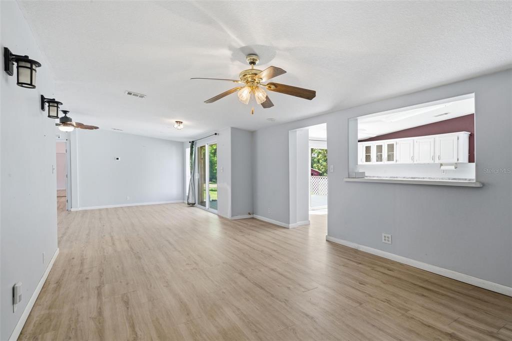 A living room with light wood-look flooring, a ceiling fan, and a kitchen pass-through window — 2295 S STONEBROOK DRIVE, HOMOSASSA, FL