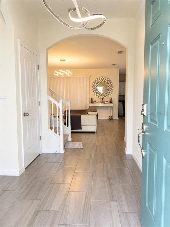 An entryway with light wood-look tile flooring leads into a living area with arched openings — 10042 SWAY STREET, WINTER GARDEN, FL