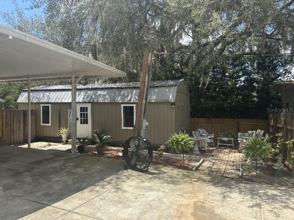 A small tan shed with a metal roof sits beside a concrete patio and carport — 16975 SE 249TH AVENUE, UMATILLA, FL