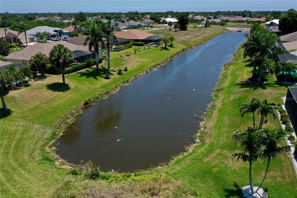 An aerial view shows a long, narrow pond surrounded by residential houses and palm trees — 23 MEDALIST CIRCLE, ROTONDA WEST, FL