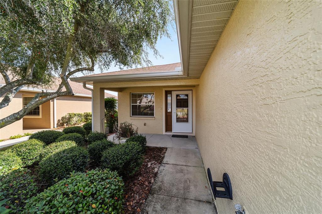 A beige stucco house features a covered entryway, a white front door, and manicured landscaping — 9150 SW 102ND CIRCLE, OCALA, FL