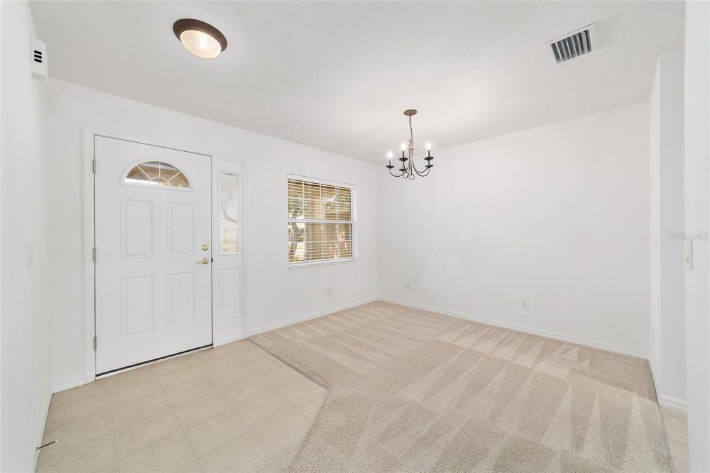 An entryway with a white front door, tiled floor, and an adjacent carpeted dining area — 9150 SW 102ND CIRCLE, OCALA, FL