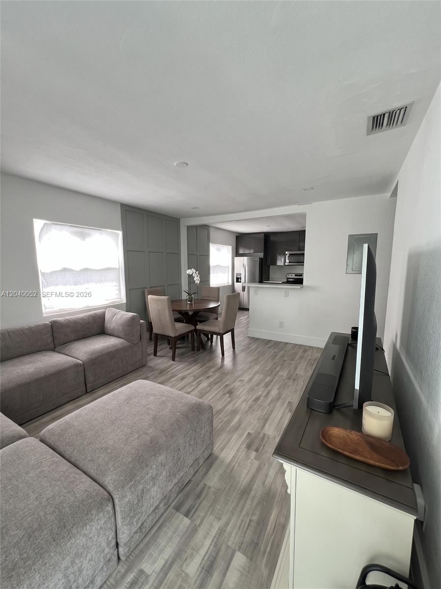 A living room and dining area feature gray wood-look flooring and a paneled accent wall — 2847 Polk St # 0, Hollywood FL 33020, HOLLYWOOD, FL