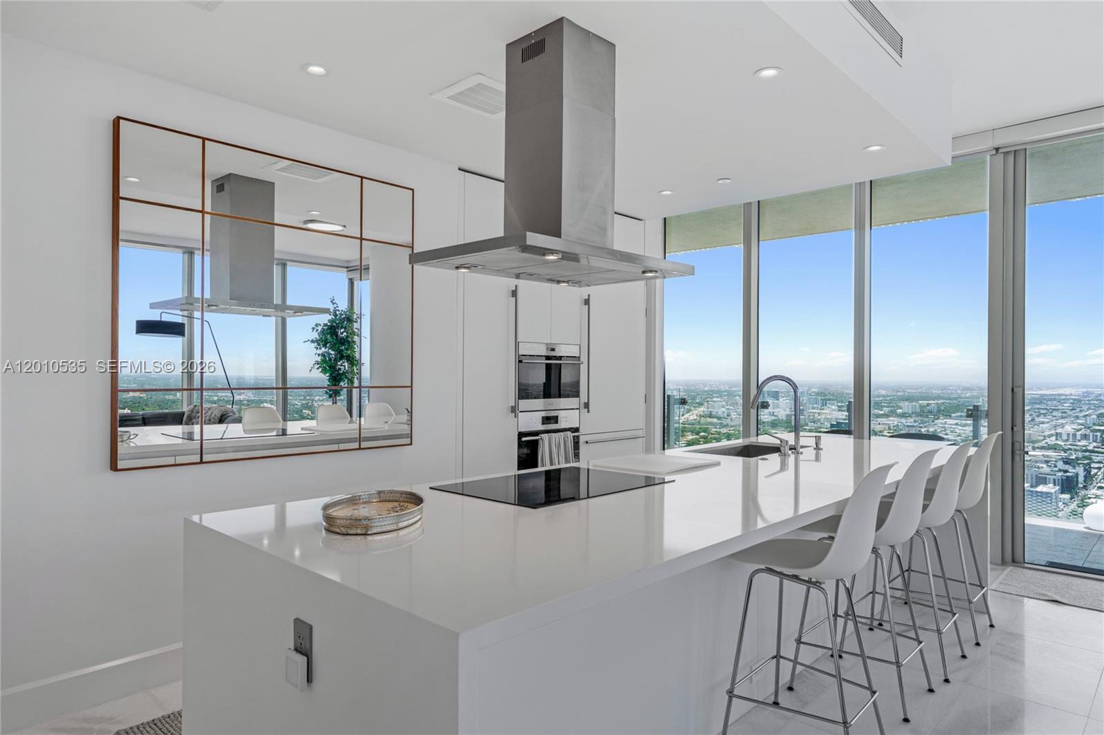 A modern white kitchen features a large island, stainless steel appliances, and floor-to-ceiling windows — 700 NE 26th Terrace # 5606, Miami FL 33137, MIAMI, FL