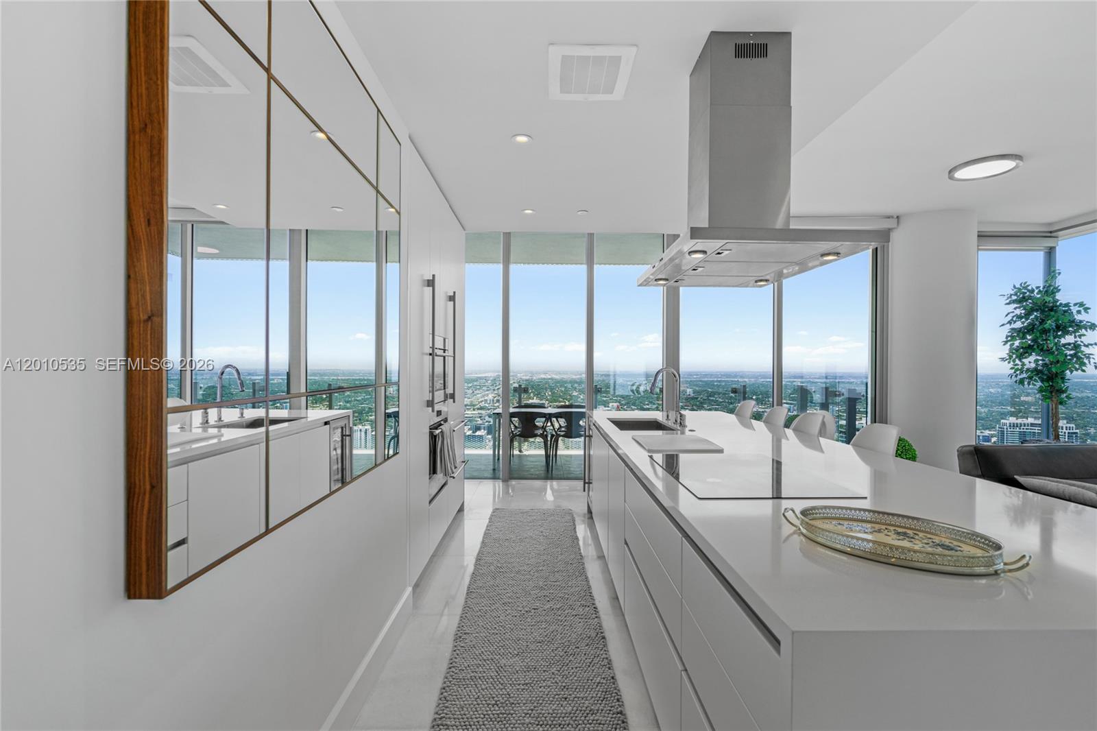 A modern kitchen features a white island, stainless steel range hood, and floor-to-ceiling windows — 700 NE 26th Terrace # 5606, Miami FL 33137, MIAMI, FL