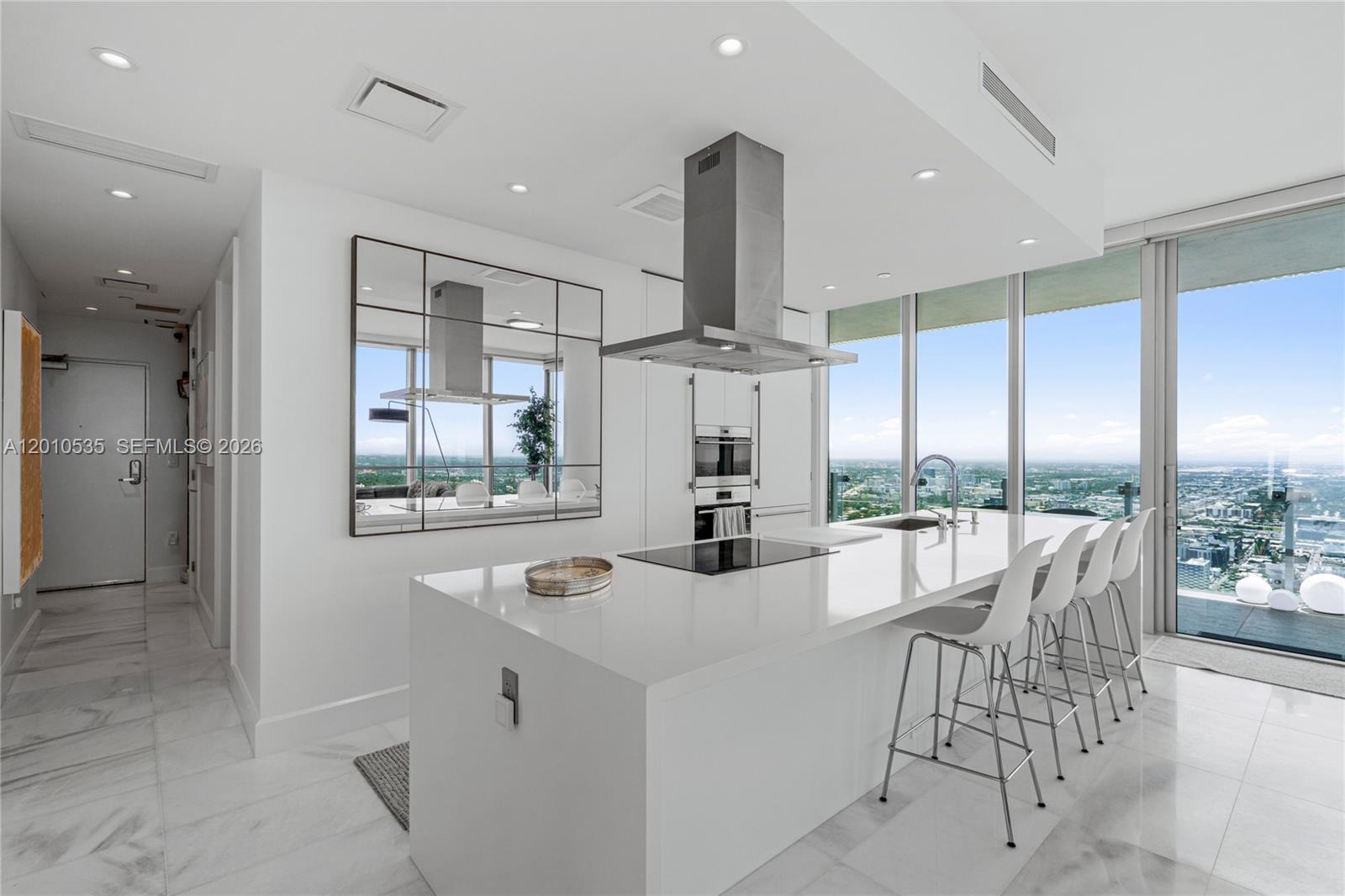 A modern white kitchen features a large island, stainless steel appliances, and floor-to-ceiling windows — 700 NE 26th Terrace # 5606, Miami FL 33137, MIAMI, FL