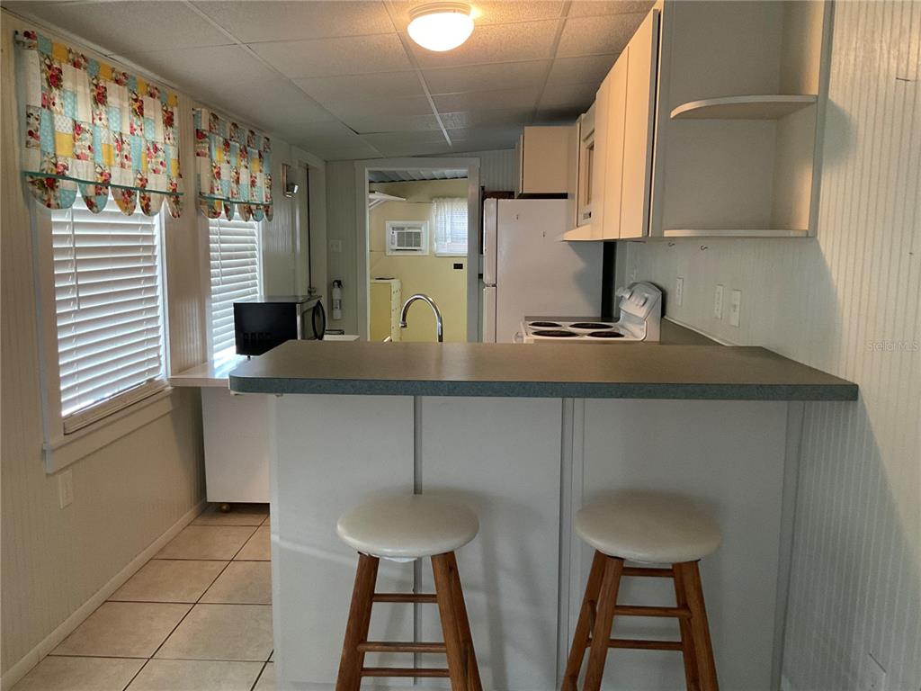 A kitchen features a breakfast bar with two stools, white cabinets, and tile flooring — 71 BULL BAY LANE UNIT 71, ENGLEWOOD, FL