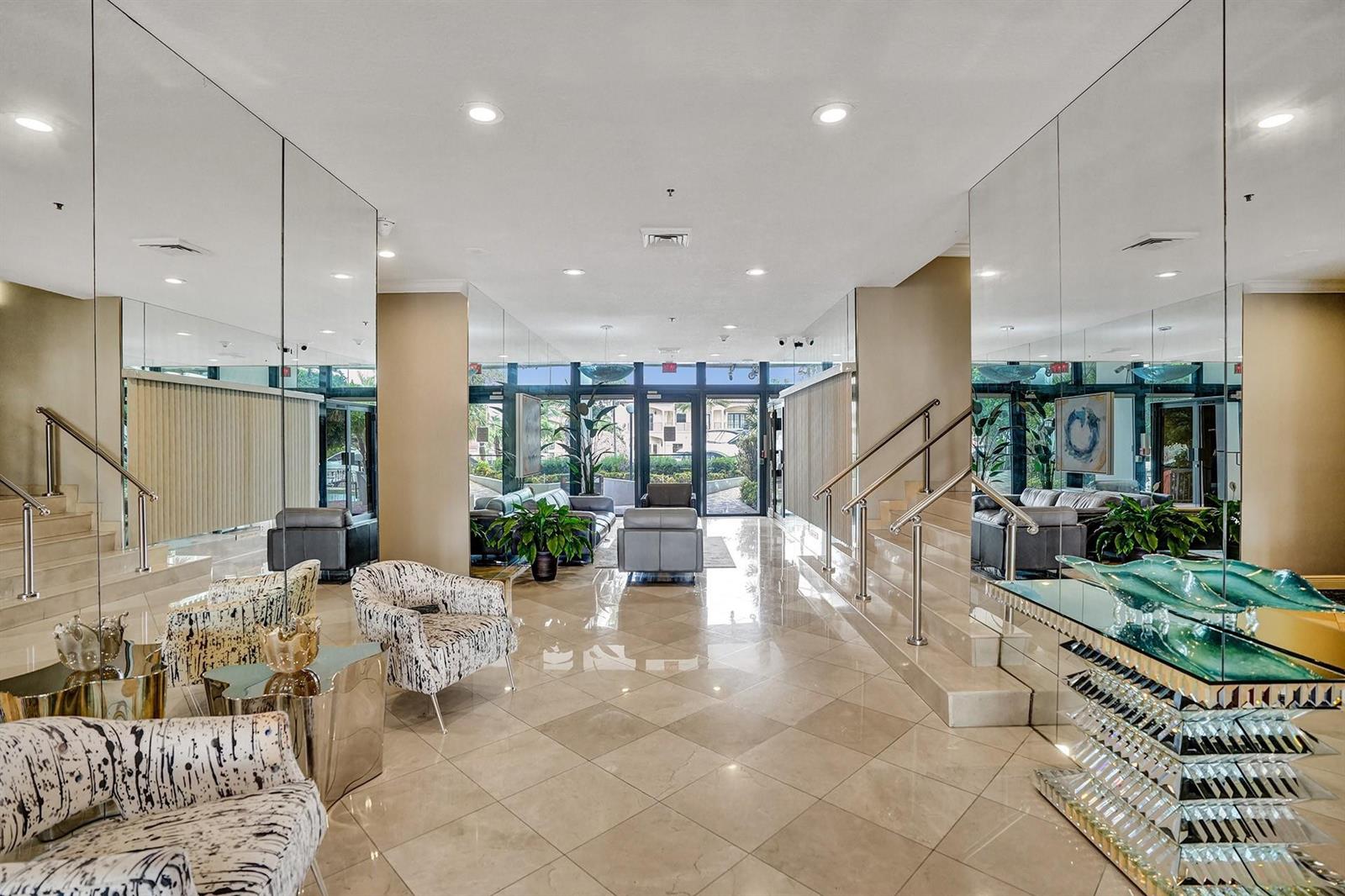 A modern lobby features mirrored walls, marble floors, two staircases, and contemporary seating areas — 1361 S Ocean Bl # 210, Pompano Beach FL 33062, POMPANO BEACH, FL