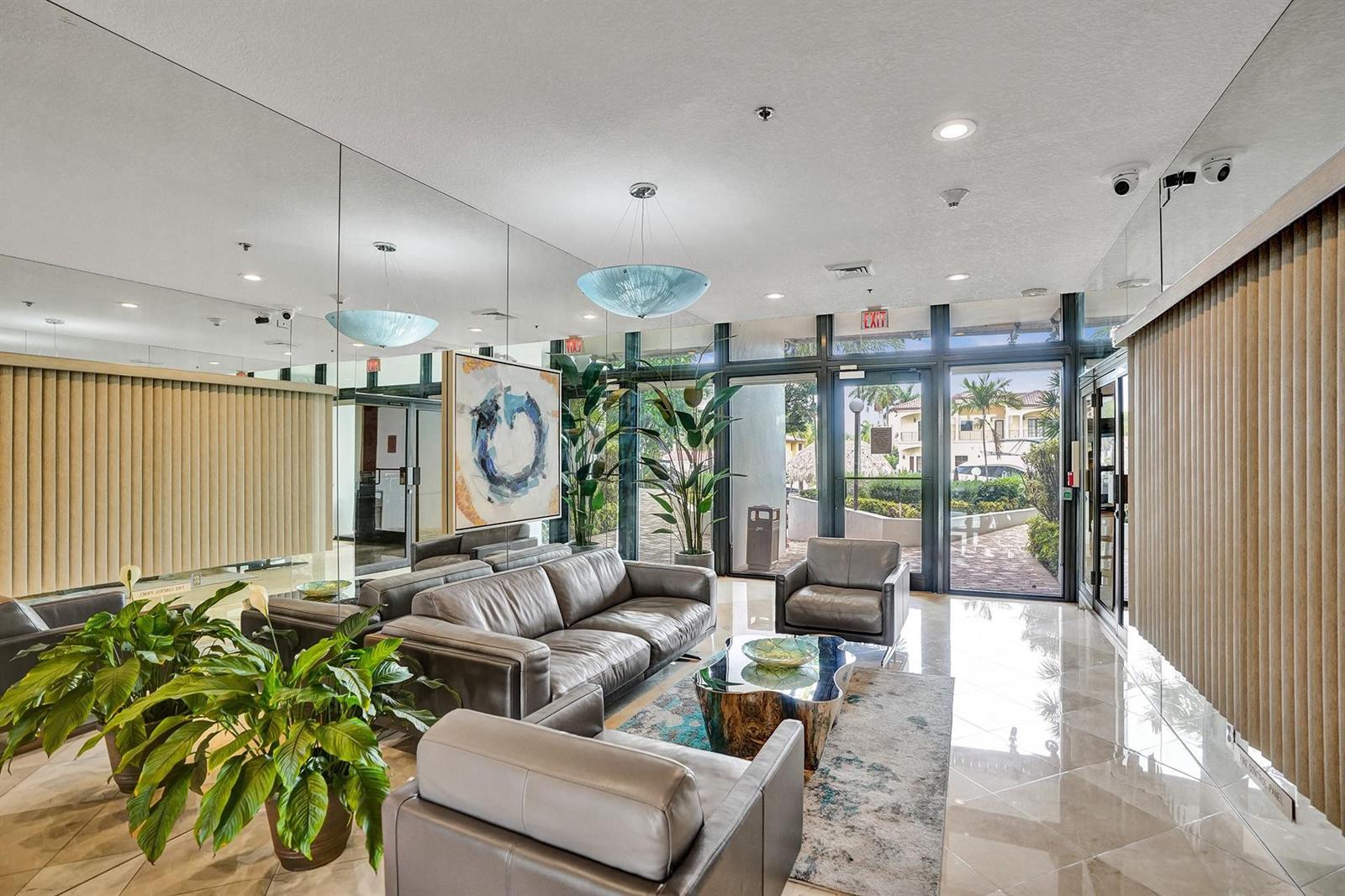 A modern lobby features leather seating, a glass coffee table, large mirrors, and potted plants — 1361 S Ocean Bl # 210, Pompano Beach FL 33062, POMPANO BEACH, FL