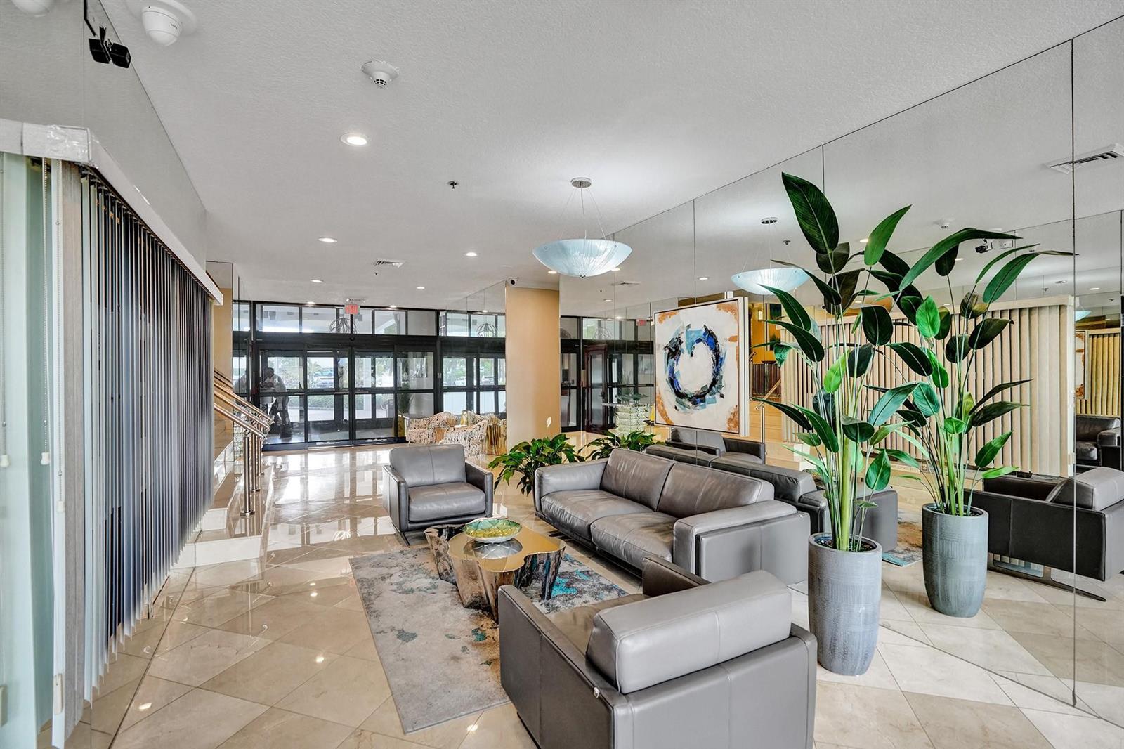 A modern lobby features gray leather seating, a metallic coffee table, and large mirrored walls — 1361 S Ocean Bl # 210, Pompano Beach FL 33062, POMPANO BEACH, FL