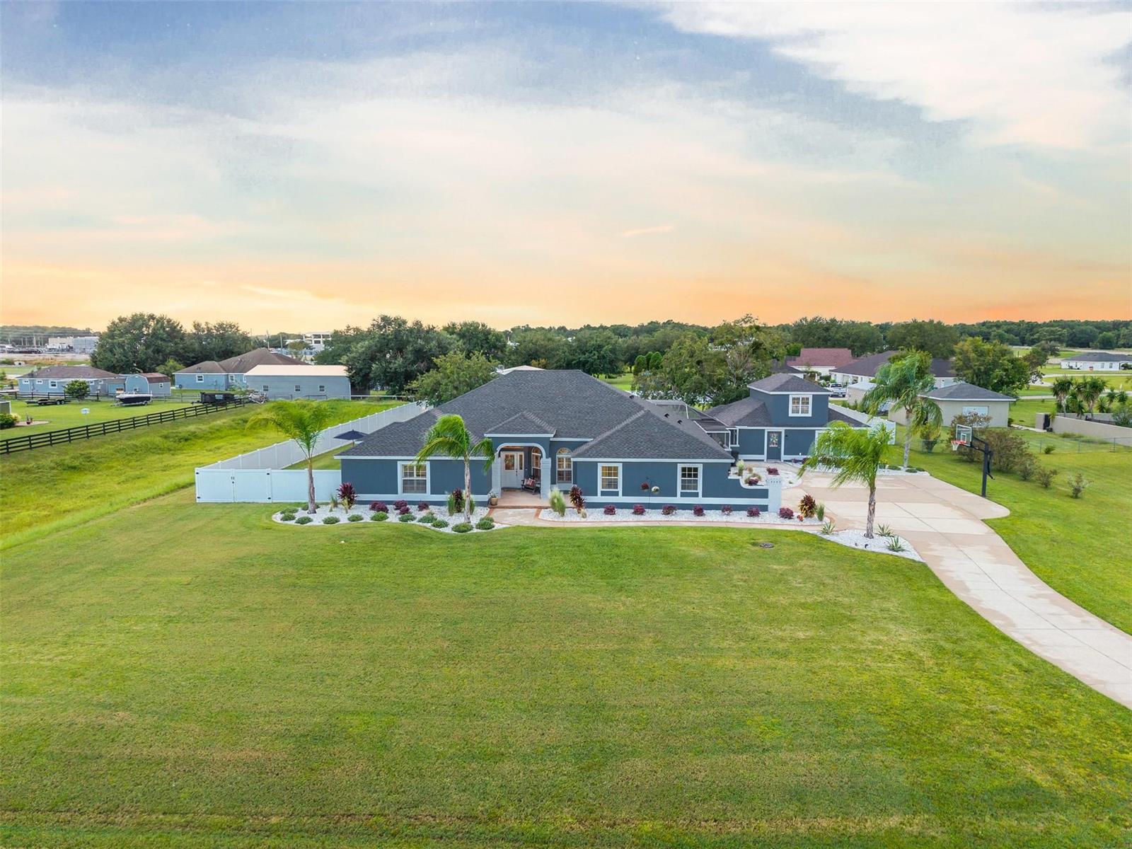 An aerial view of a dark blue, single-story house with a large lawn and driveway — 9060 County Road 128c, Wildwood FL 34785, WILDWOOD, FL