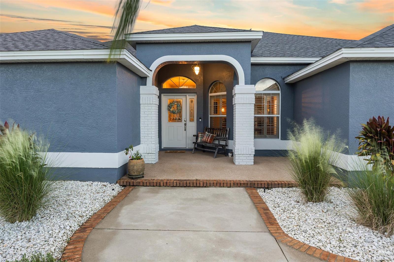 A blue house with a white-trimmed arched entryway, a concrete walkway, and decorative landscaping — 9060 County Road 128c, Wildwood FL 34785, WILDWOOD, FL