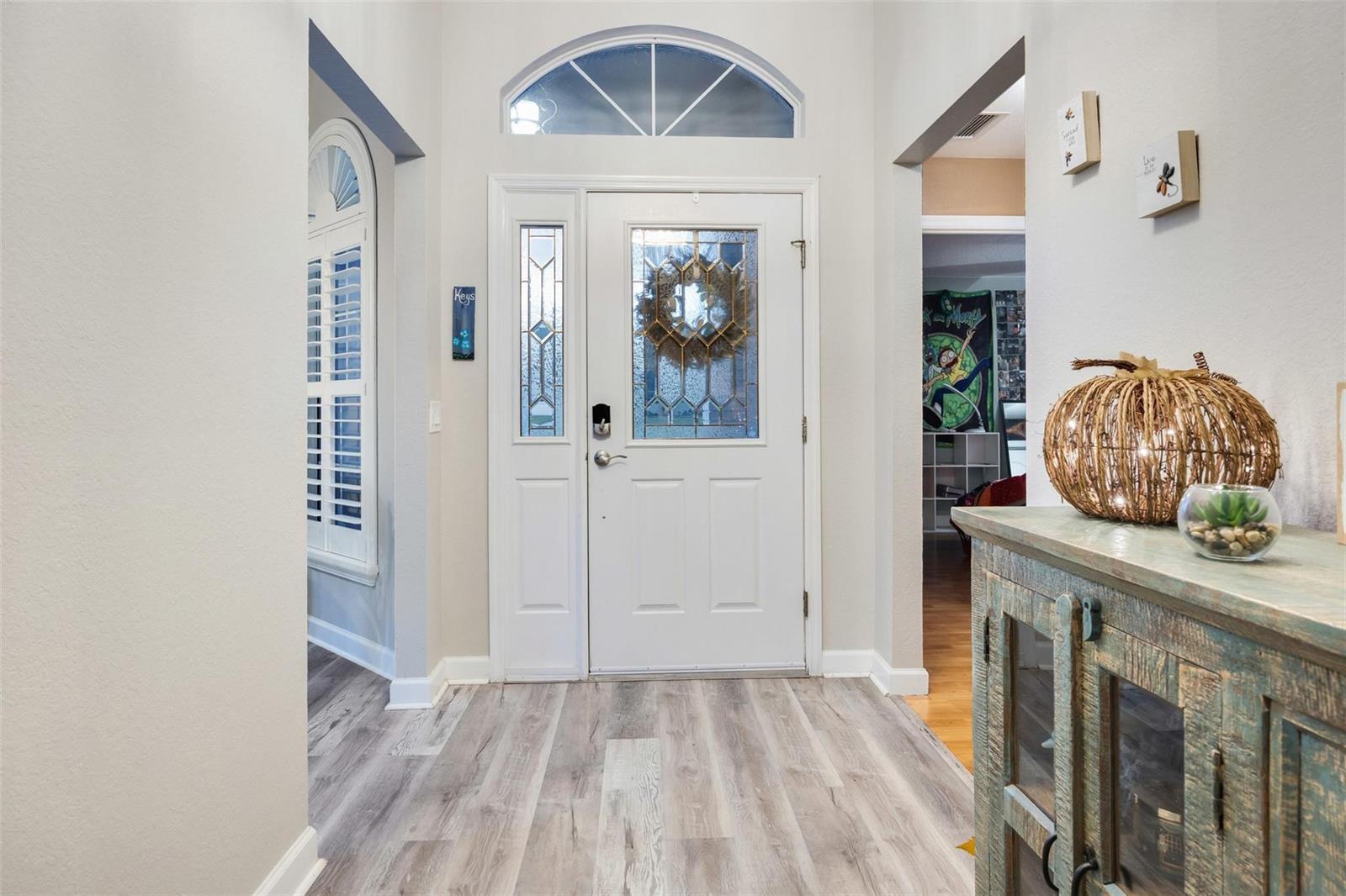 A bright entryway features a white front door with a transom window and wood-look flooring — 9060 County Road 128c, Wildwood FL 34785, WILDWOOD, FL