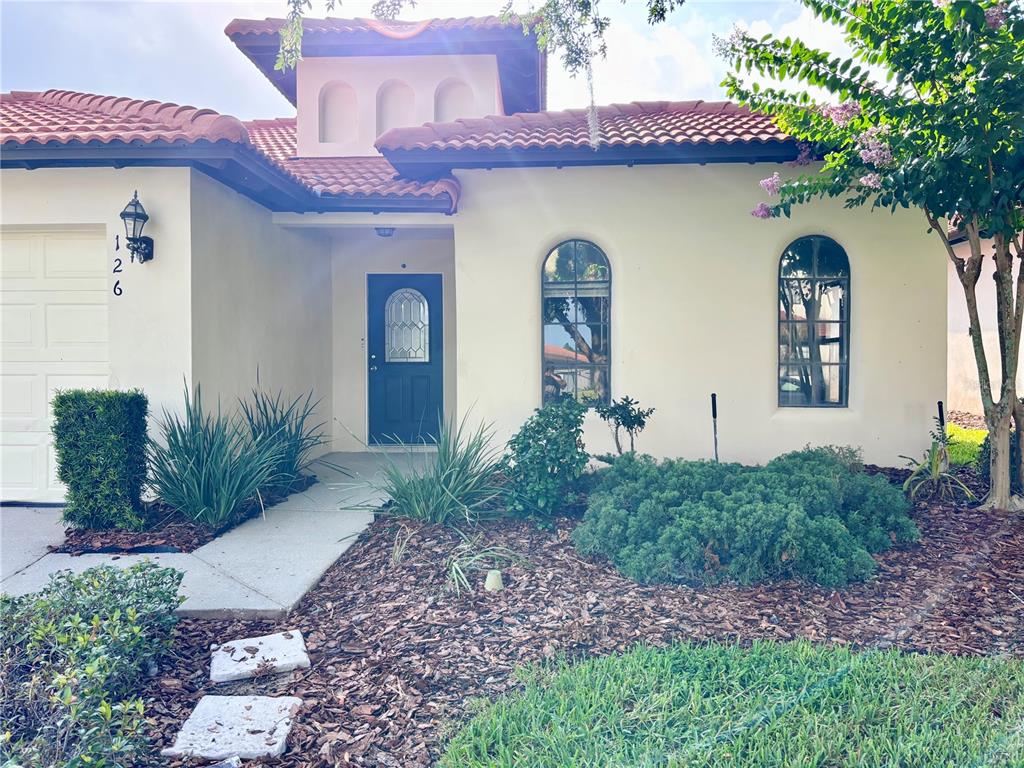 The exterior of a stucco house features a tiled roof, arched windows, and a dark door — 126 SANDY POINT WAY, CLERMONT, FL