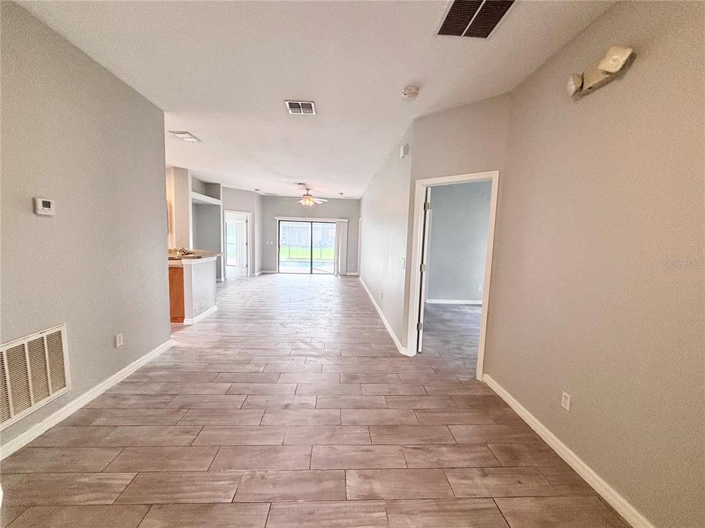 An open-concept living area features light gray walls, wood-look tile flooring, and a sliding glass door — 126 SANDY POINT WAY, CLERMONT, FL