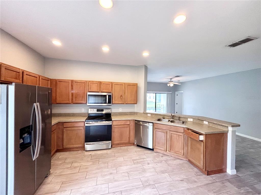 A kitchen features wood cabinets, stainless steel appliances, and light-colored tile flooring — 126 SANDY POINT WAY, CLERMONT, FL
