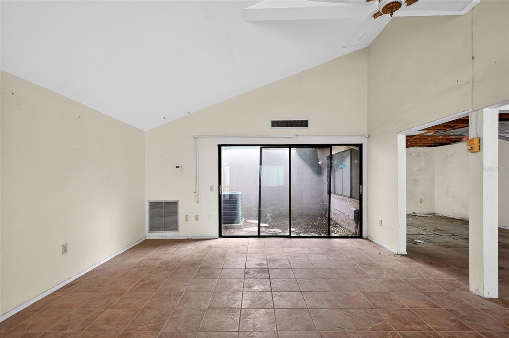 A room with tiled floors, a vaulted ceiling, and sliding glass doors leading to a courtyard — 12521 MERRY LANE, HUDSON, FL