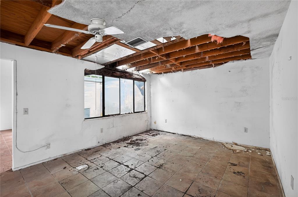 A damaged room with exposed ceiling joists, missing drywall, and debris on the tiled floor — 12521 MERRY LANE, HUDSON, FL