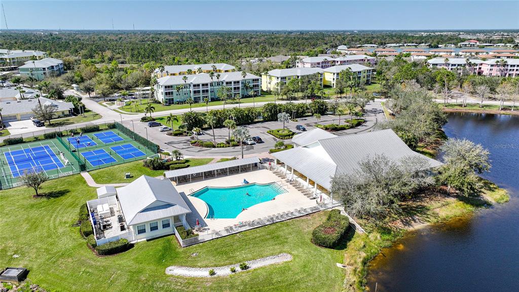 An aerial view shows a community pool, tennis courts, and apartment buildings near a lake — 2061 WILLOW HAMMOCK CIRCLE UNIT 105, PUNTA GORDA, FL