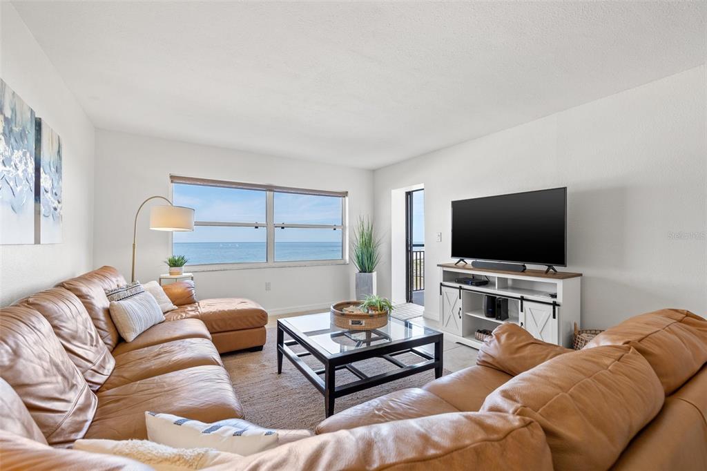 A living room features two tan leather sofas, a glass coffee table, and ocean views — 1270 GULF BOULEVARD UNIT 1007, CLEARWATER BEACH, FL
