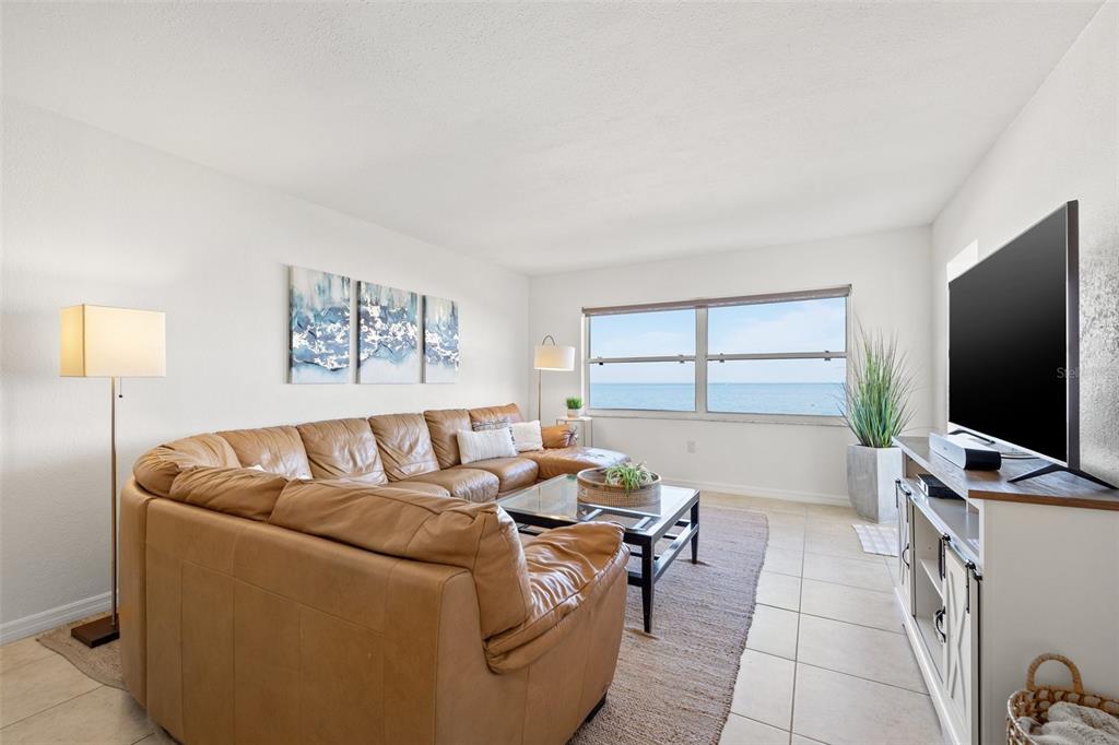 A living room features a tan leather sectional, a glass coffee table, and ocean views — 1270 GULF BOULEVARD UNIT 1007, CLEARWATER BEACH, FL