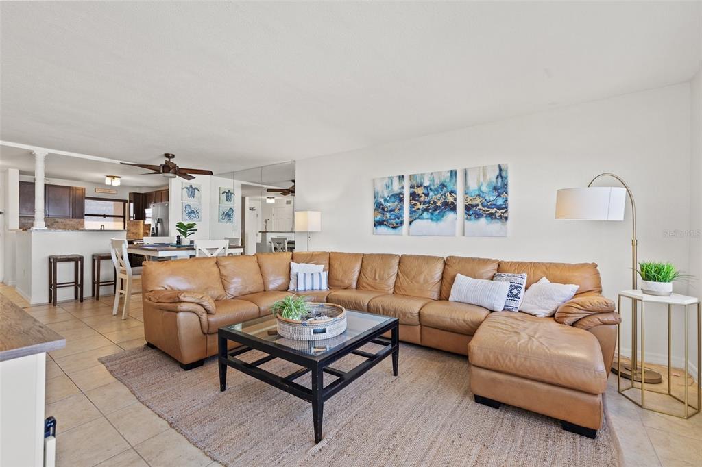 A living room features a large tan leather sectional, a glass-topped coffee table, and artwork — 1270 GULF BOULEVARD UNIT 1007, CLEARWATER BEACH, FL