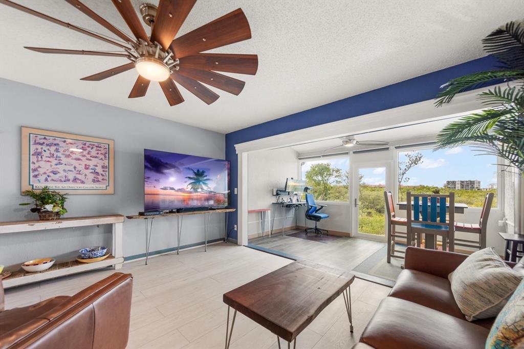 A living room features a ceiling fan, a television, and an adjacent sunroom with views — 9434 TARA CAY COURT UNIT 25, SEMINOLE, FL