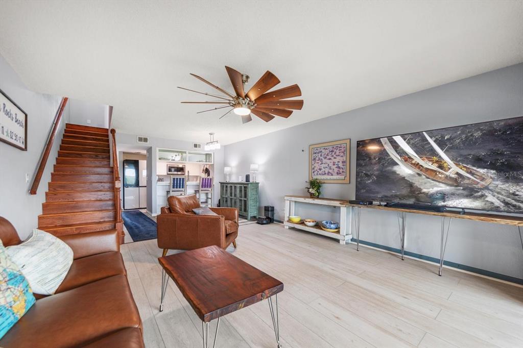 A living room features a wooden staircase, leather furniture, a ceiling fan, and a television — 9434 TARA CAY COURT UNIT 25, SEMINOLE, FL