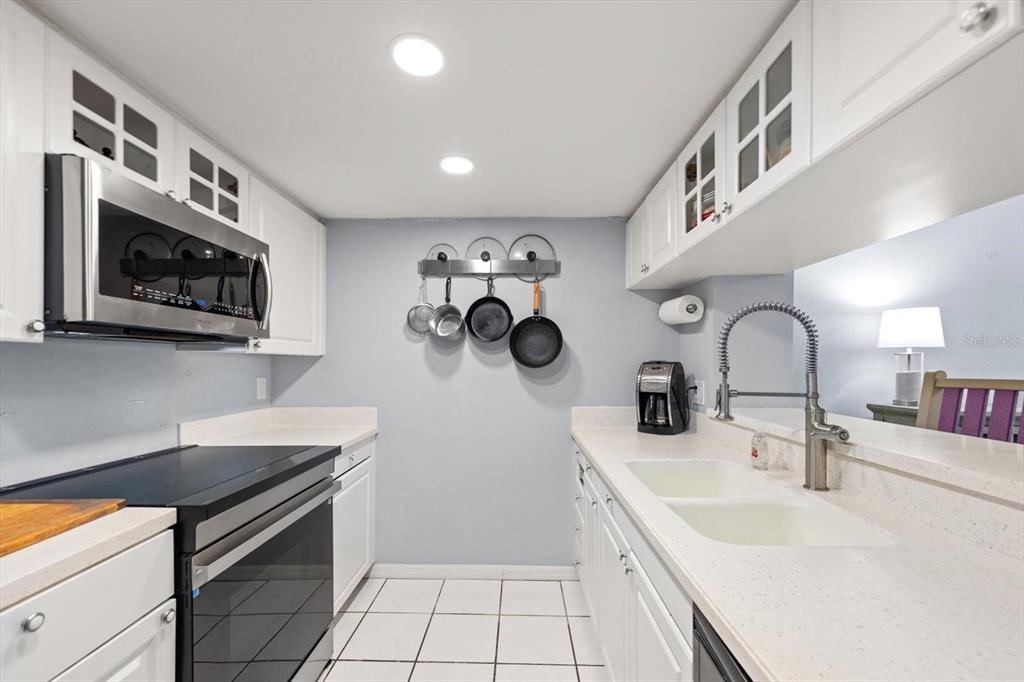 A galley kitchen features white cabinets, stainless steel appliances, a double sink, and tiled floors — 9434 TARA CAY COURT UNIT 25, SEMINOLE, FL