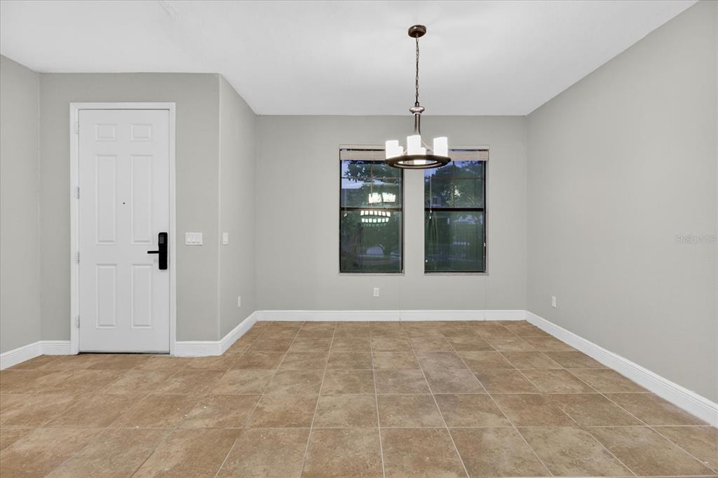 An empty dining room features light gray walls, tile flooring, and a central chandelier — 1389 HERITAGE LANDINGS DRIVE, LAKELAND, FL
