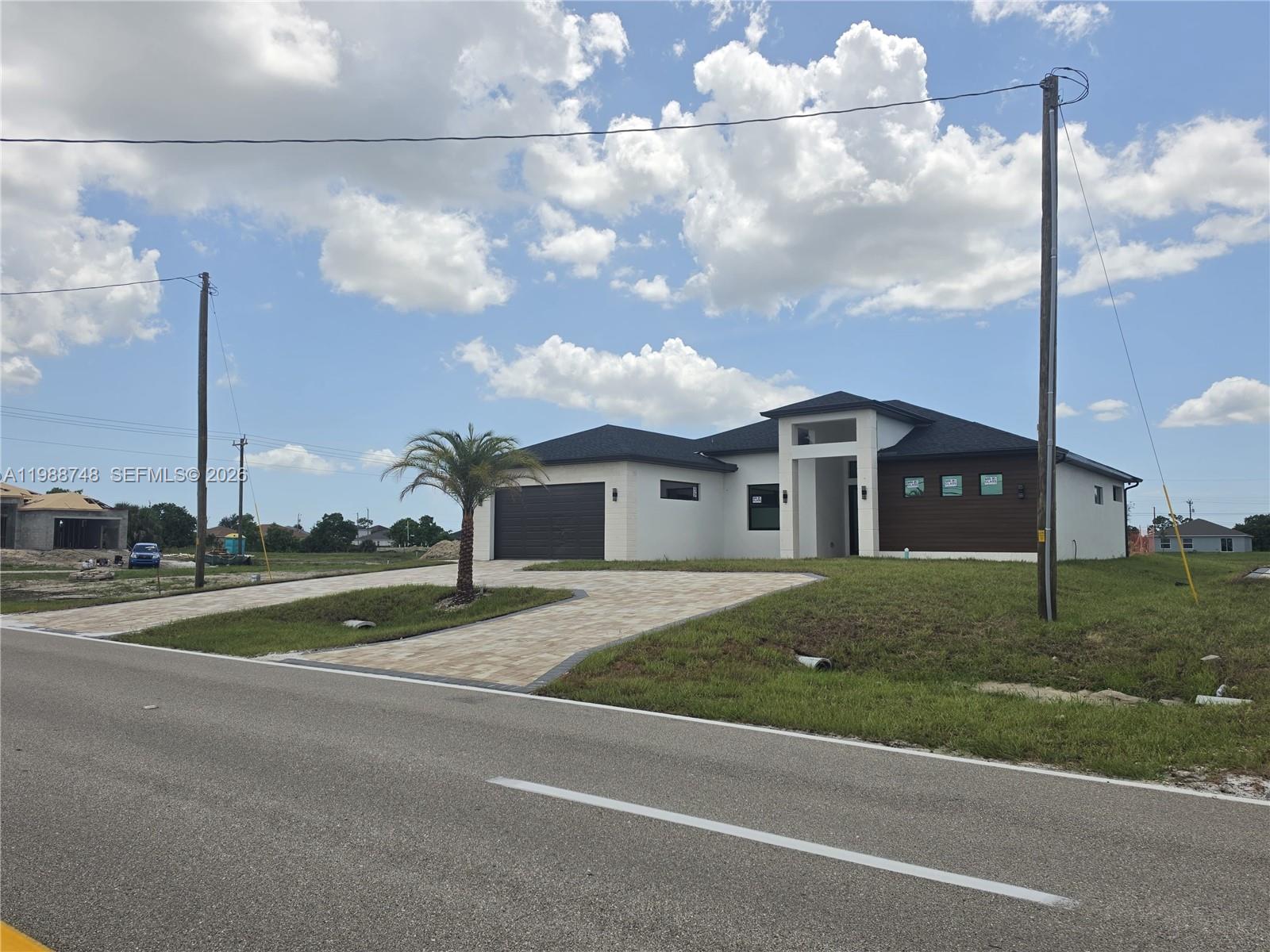 A modern, single-story house with a white exterior, dark wood accents, and a paved driveway — 2006 Nelson RD N, Cape Coral FL 33993, CAPE CORAL, FL