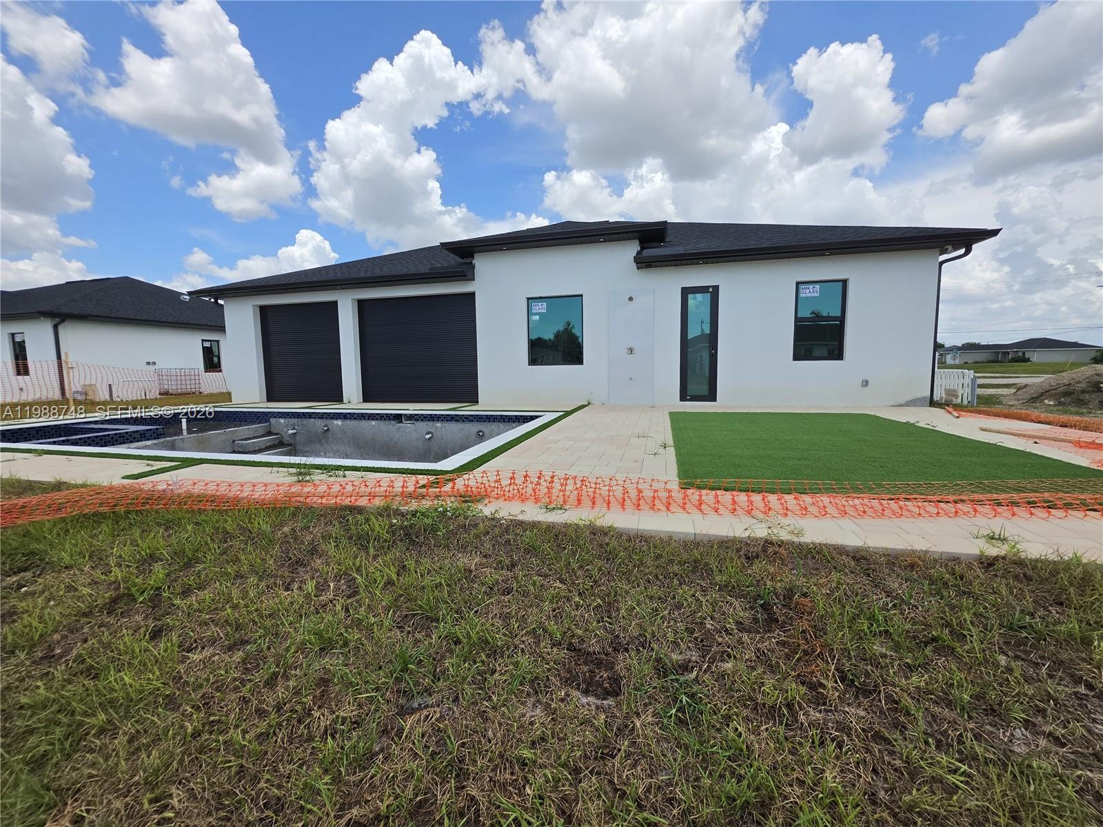 A modern white house exterior features a swimming pool, artificial turf, and black garage doors — 2006 Nelson RD N, Cape Coral FL 33993, CAPE CORAL, FL