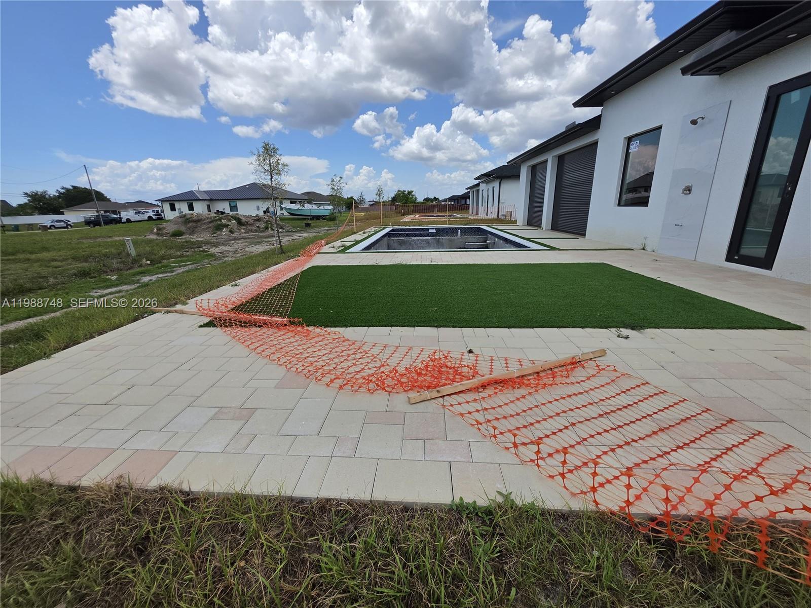 A backyard features a rectangular swimming pool, artificial turf, and light-colored pavers under construction — 2006 Nelson RD N, Cape Coral FL 33993, CAPE CORAL, FL