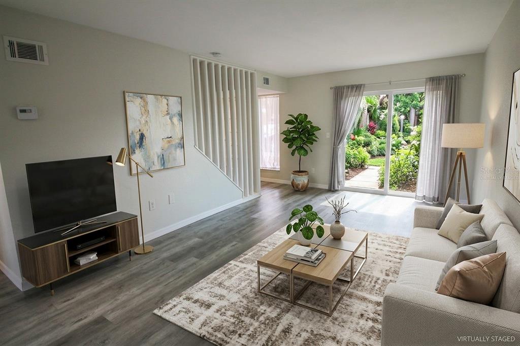 This virtually staged living room features wood-look flooring, a sliding glass door, and stairs — 1836 N CRYSTAL LAKE DRIVE UNIT 68, LAKELAND, FL