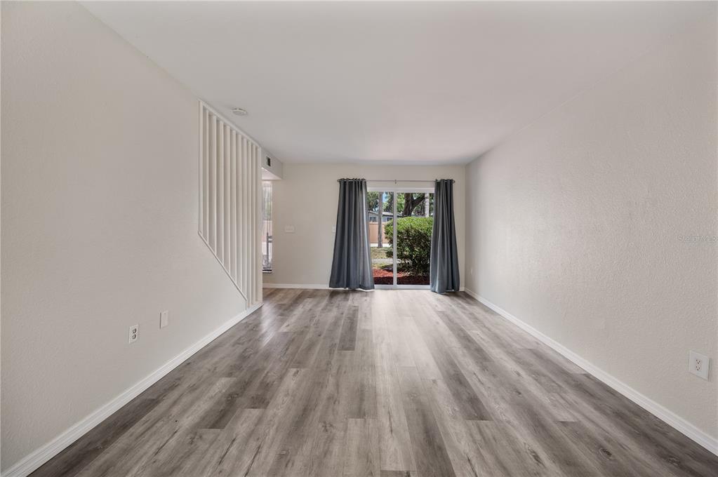 An empty room features light gray wood-look flooring, white walls, and a sliding glass door — 1836 N CRYSTAL LAKE DRIVE UNIT 68, LAKELAND, FL