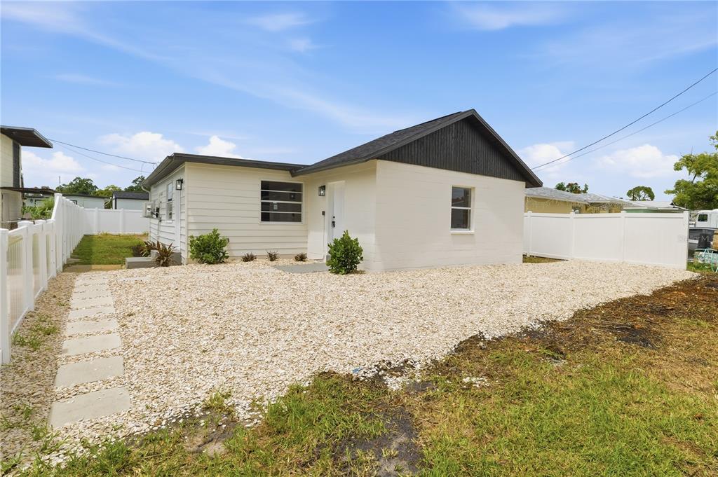 A white single-story house with a gravel yard and a white vinyl fence — 3923 W FLORA STREET, TAMPA, FL