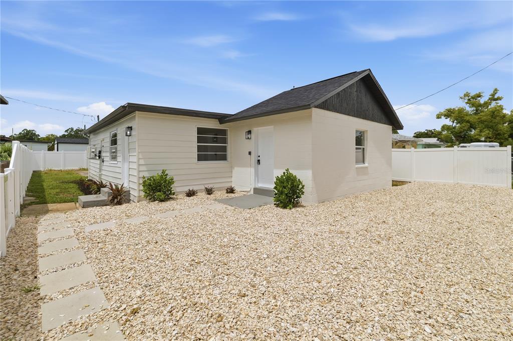 A single-story house with white siding and a gravel front yard enclosed by white fencing — 3923 W FLORA STREET, TAMPA, FL
