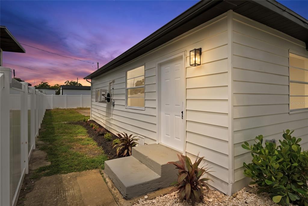 The exterior of a white house features a side door, concrete steps, and a fence — 3923 W FLORA STREET, TAMPA, FL