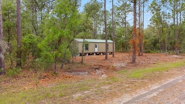 A small, tan mobile home sits on a wooded lot near a dirt road — 10890 SE 133RD AVENUE, DUNNELLON, FL