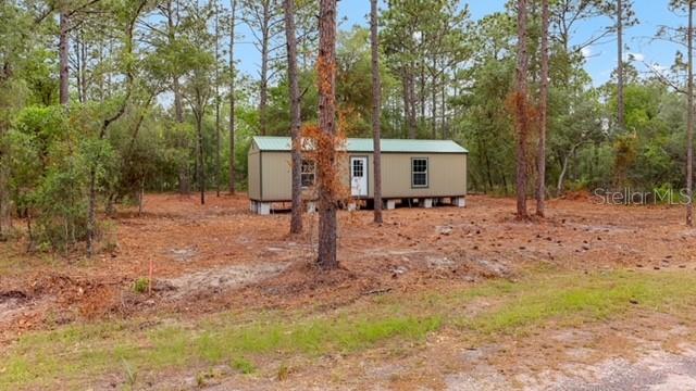 A tan mobile home sits on a wooded lot with a green metal roof — 10890 SE 133RD AVENUE, DUNNELLON, FL