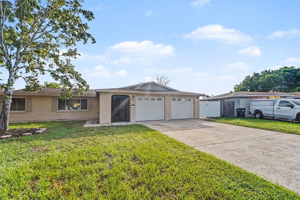 A single-story house with a two-car garage, a concrete driveway, and a large tree — 5751 DOLORES DRIVE, HOLIDAY, FL